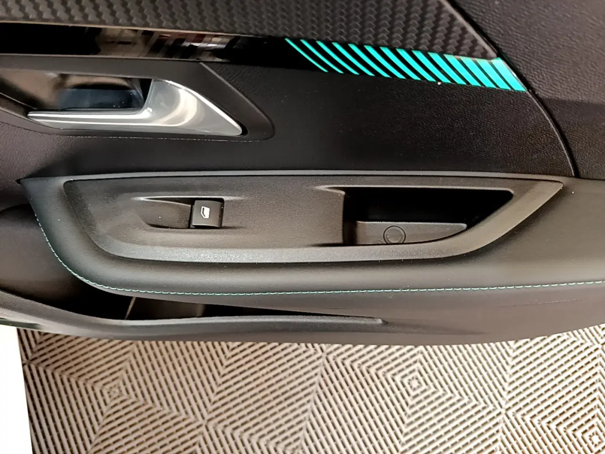 Détail de la porte intérieure côté conducteur de la Peugeot 208 blanche avec surpiqûres bleues et poignée argentée.