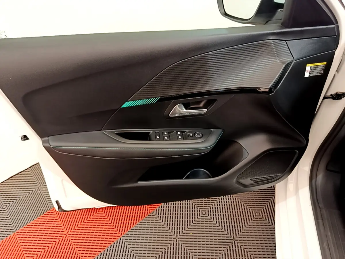 Vue côté gauche de la porte avant blanche d'une Peugeot 208 2020, avec garniture noire et insert effet carbone.