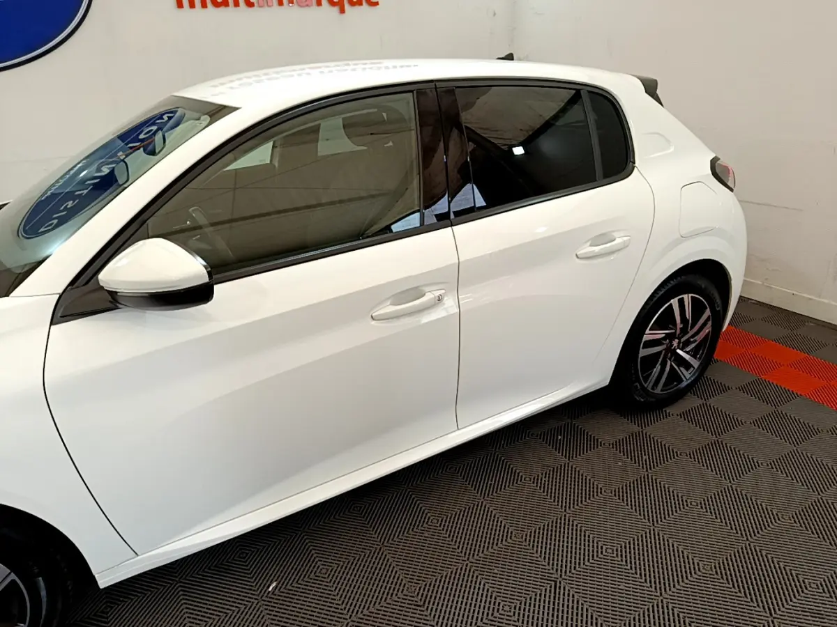 Profil côté gauche d'une Peugeot 208 blanche PureTech 100 S&S Allure Business, avec jantes alliage et vitres teintées.