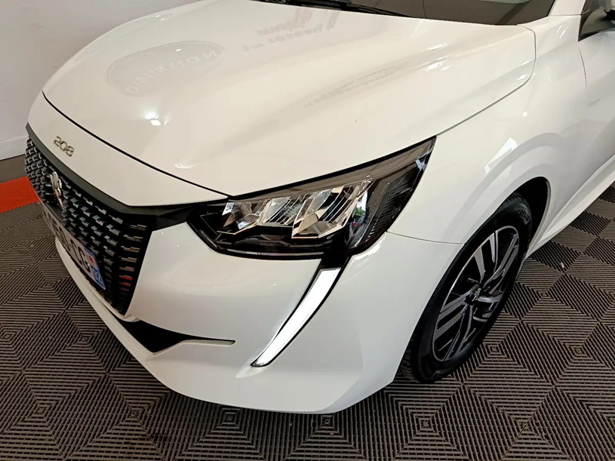 Vue 3/4 avant droit d'une Peugeot 208 blanche avec phares LED et calandre noire distinctive.