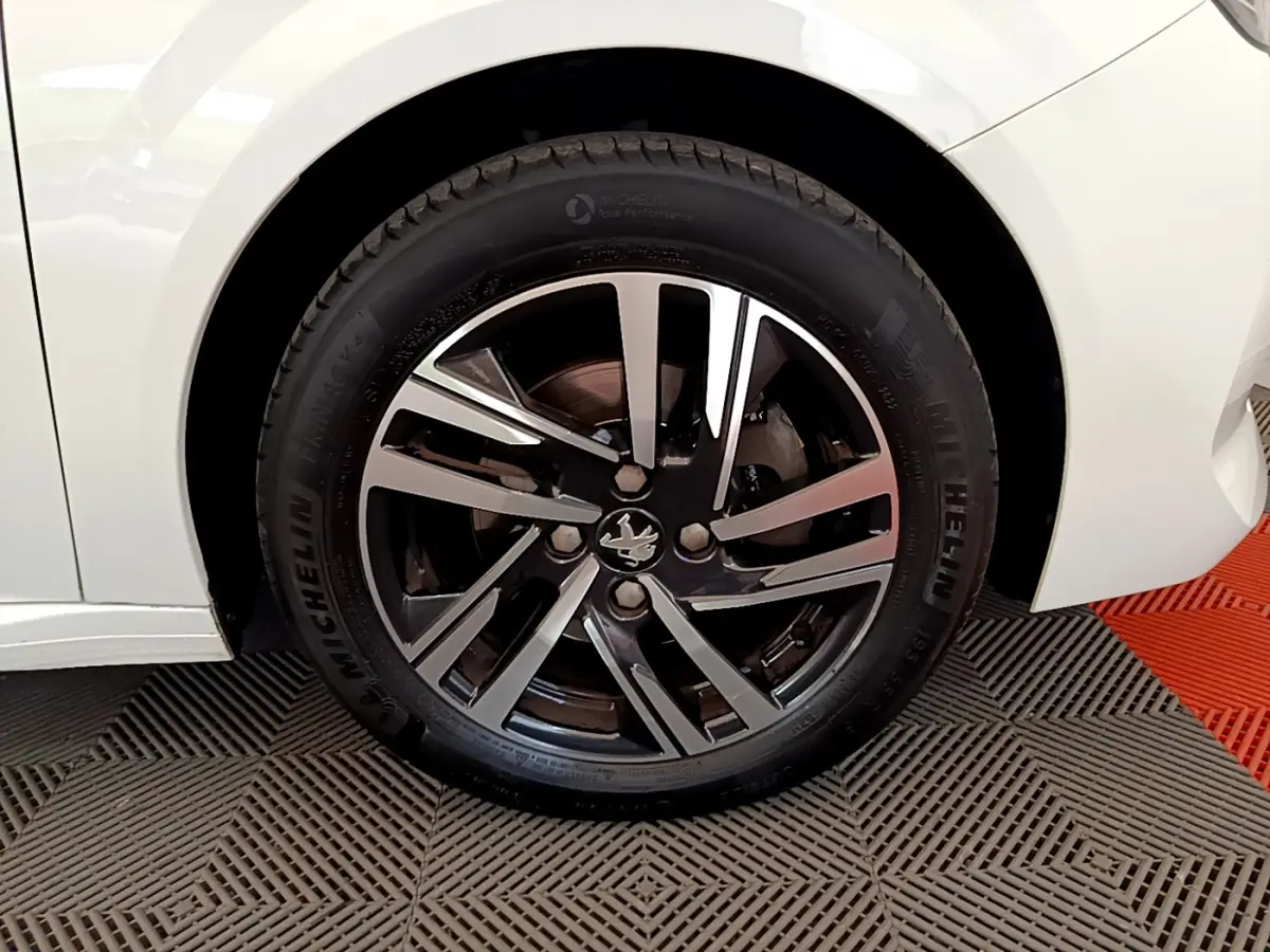 Gros plan sur la roue avant gauche blanche d'une Peugeot 208 avec jante alliage noire et argentée au design moderne.