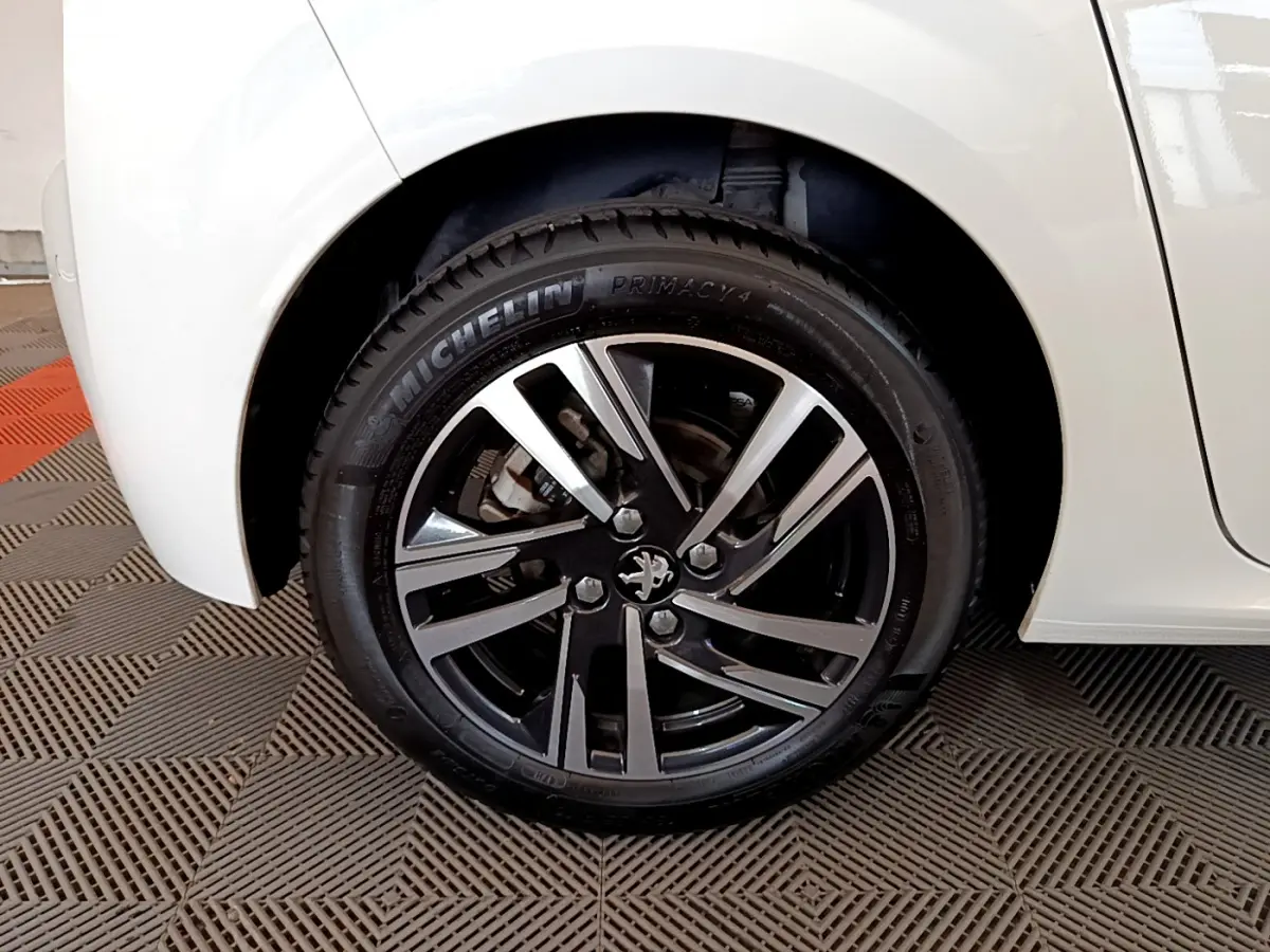 Gros plan sur la roue arrière droite blanche d'une Peugeot 208 PureTech 100 S&S Allure Business avec jante alliage noire et argent.