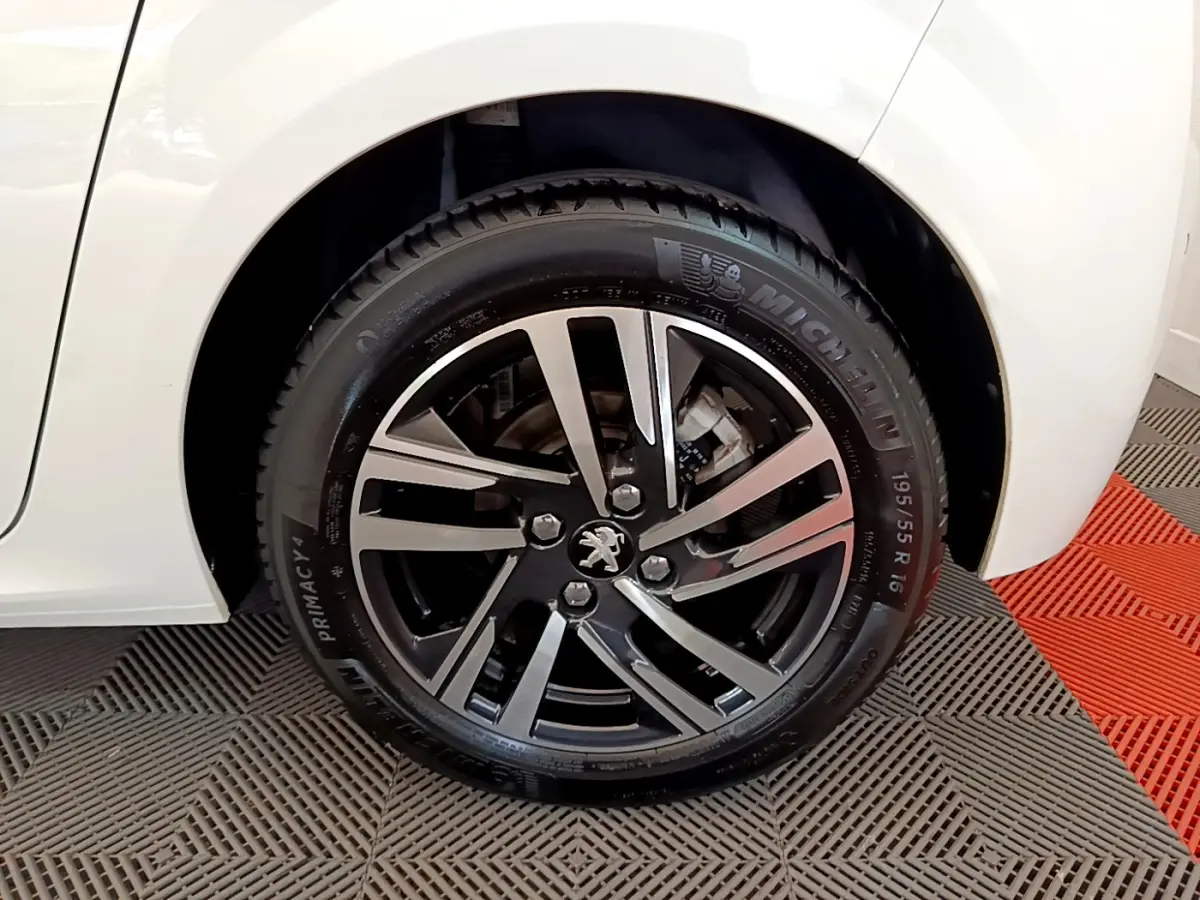 Gros plan sur la roue avant gauche d'une Peugeot 208 blanche avec jante alliage noire et argentée.