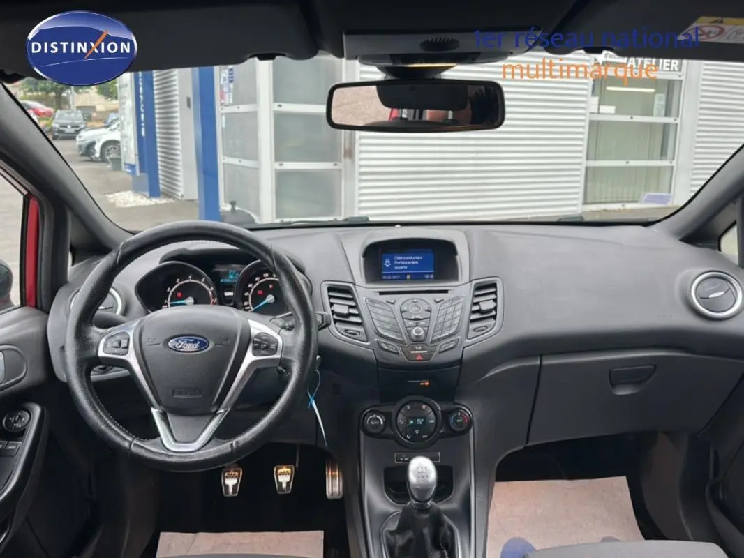 Vue intérieure avant de la Ford Fiesta rouge 2017, tableau de bord avec volant multifonction et boîte manuelle.
