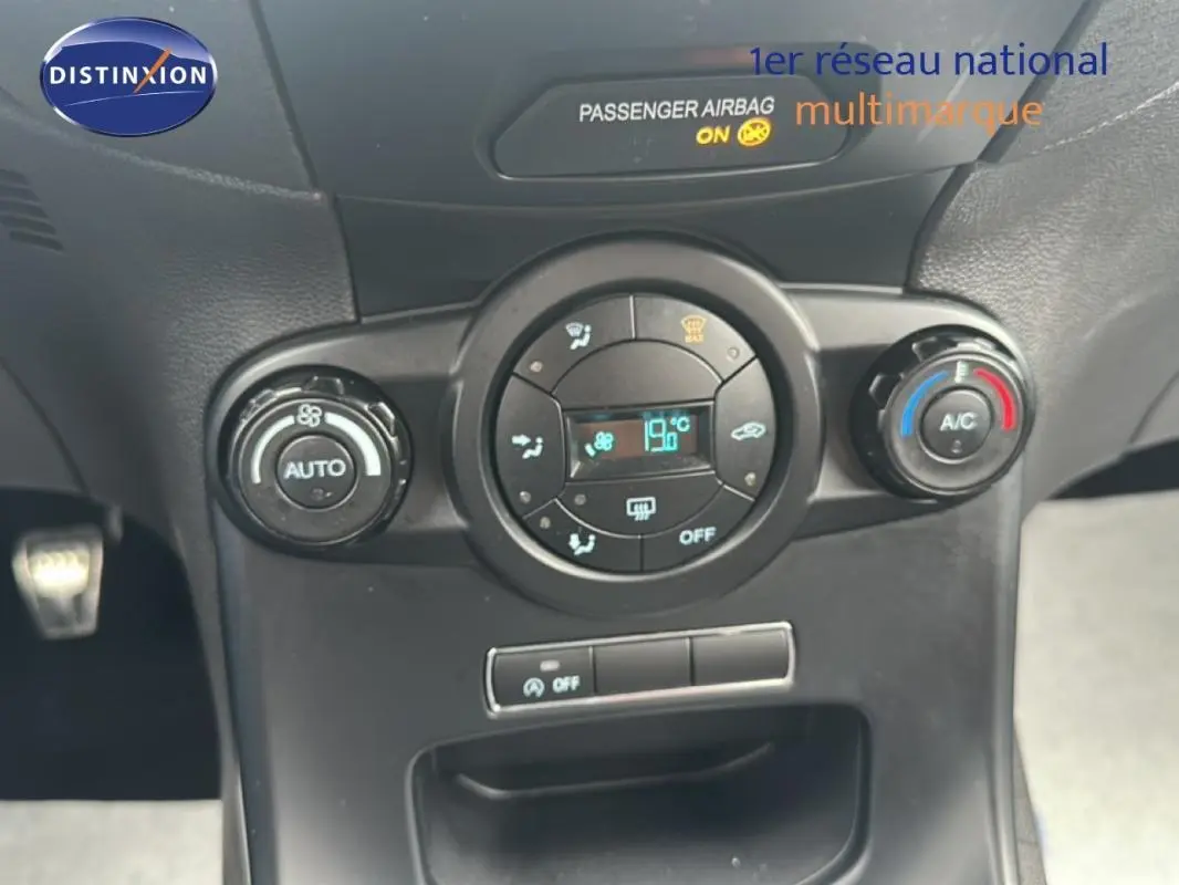 Vue rapprochée du tableau de bord central de la Ford Fiesta rouge 2017, avec commandes climatisation et affichage digital.