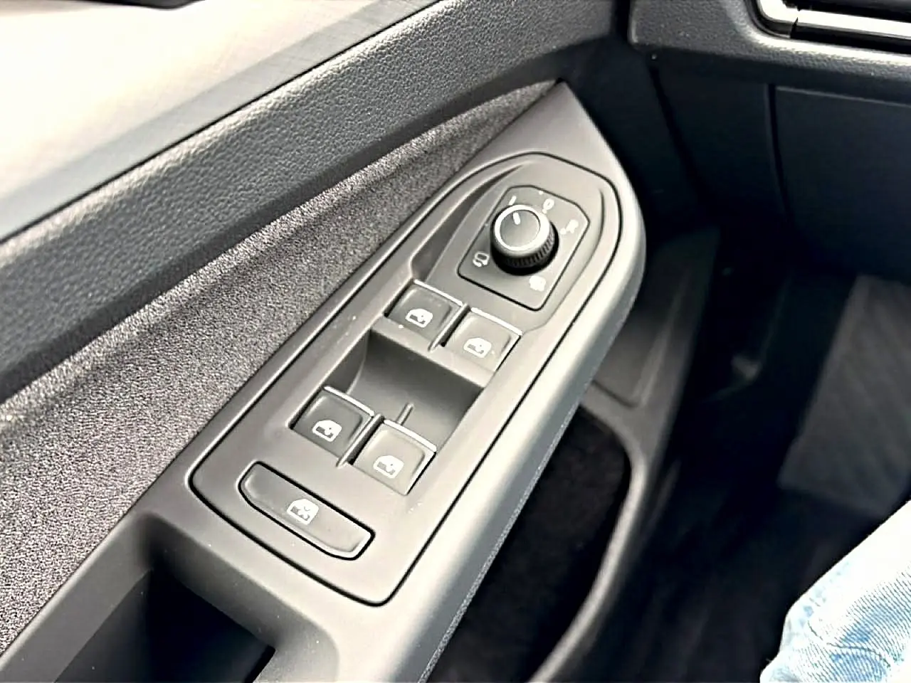 Gros plan sur les commandes de lève-vitres et rétroviseurs côté conducteur d'une Volkswagen Golf 2026, intérieur noir.