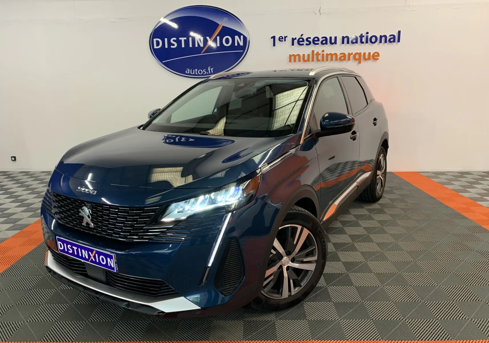 Vue 3/4 avant d'un Peugeot 3008 PureTech 130 Allure Pack bleu Célèbes avec phares allumés en showroom.
