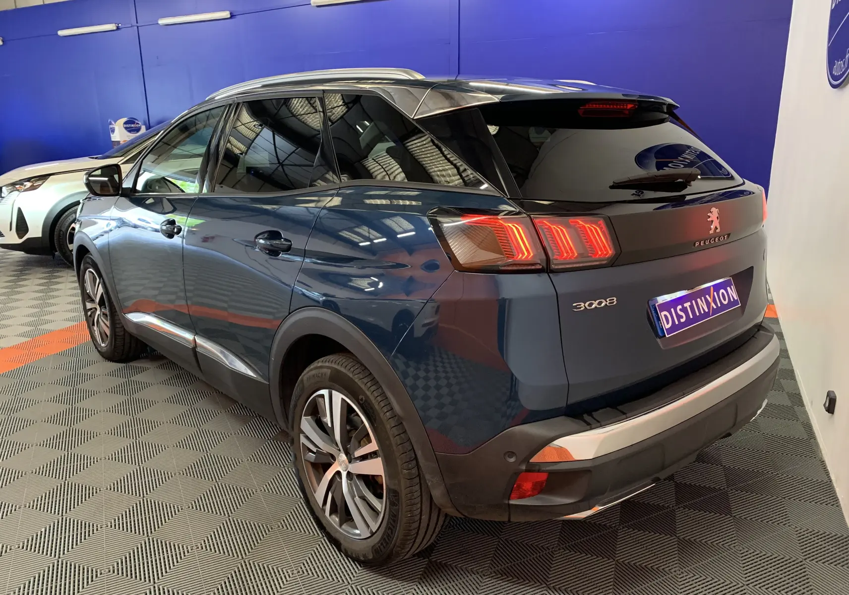 Vue 3/4 arrière droite d'un Peugeot 3008 bleu Célèbes avec feux arrière allumés dans un showroom.