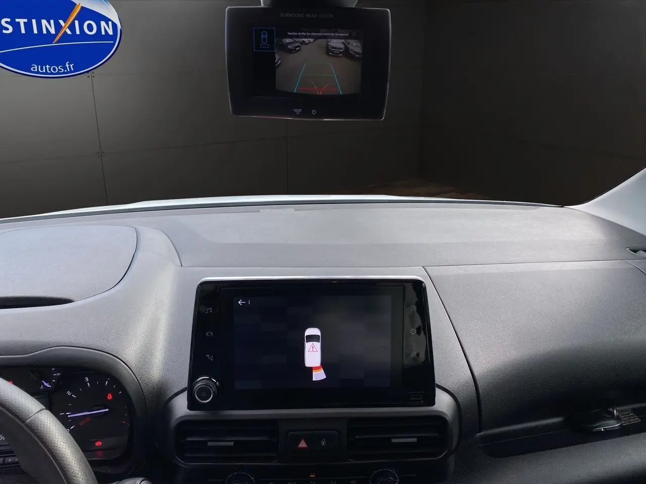 Vue intérieure du tableau de bord du Citroën Berlingo blanc, avec écran tactile affichant l'aide au stationnement et caméra de recul.