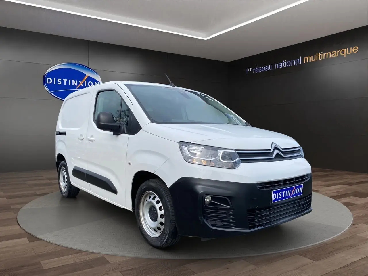 Vue 3/4 avant d'un Citroën Berlingo blanc 2019 avec pare-chocs noir et jantes acier en présentation showroom.