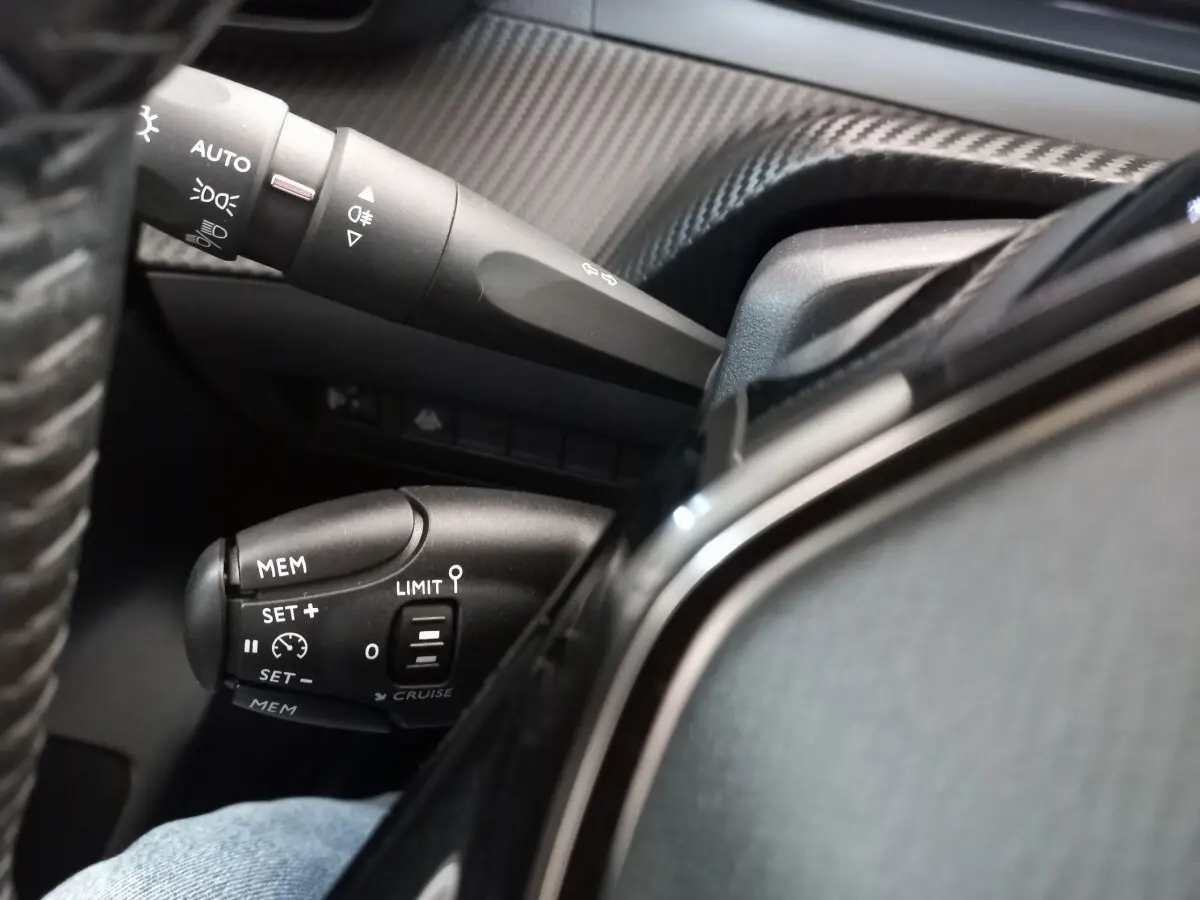 Gros plan sur les commandes de régulateur de vitesse et feux au volant cuir d'une Peugeot 208 PureTech blanche.