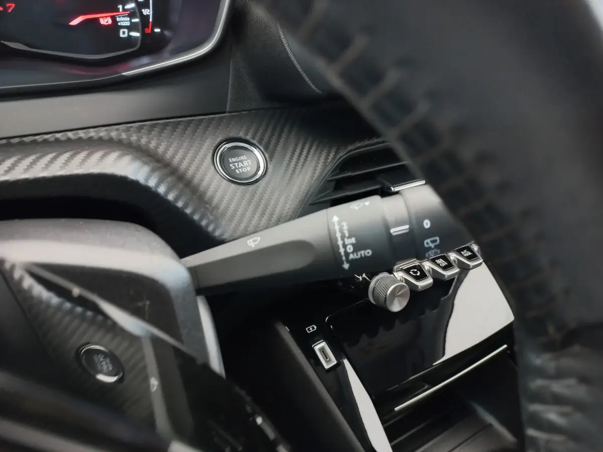 Gros plan sur le bouton start/stop et la commande d'essuie-glace dans l'habitacle noir du Peugeot 208 PureTech 100 S&S Allure 2021.
