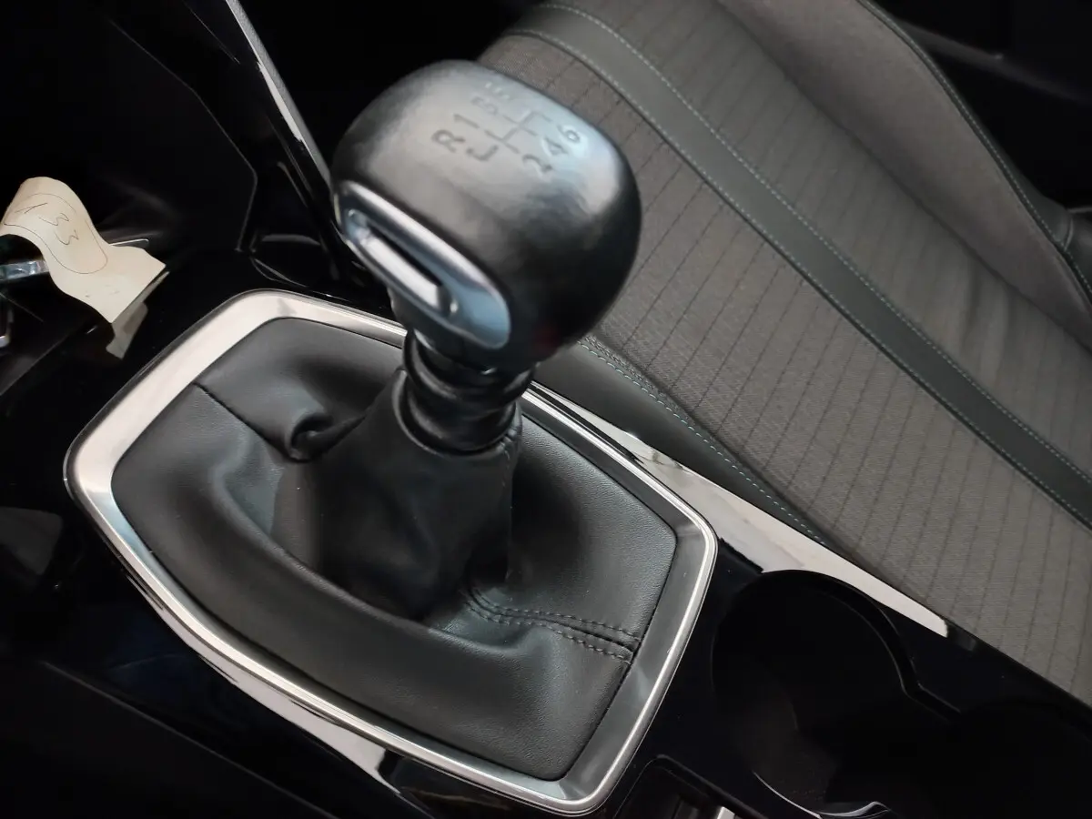 Gros plan sur le levier de vitesse manuel noir et la sellerie grise du siège avant droit d'une Peugeot 208 blanche.