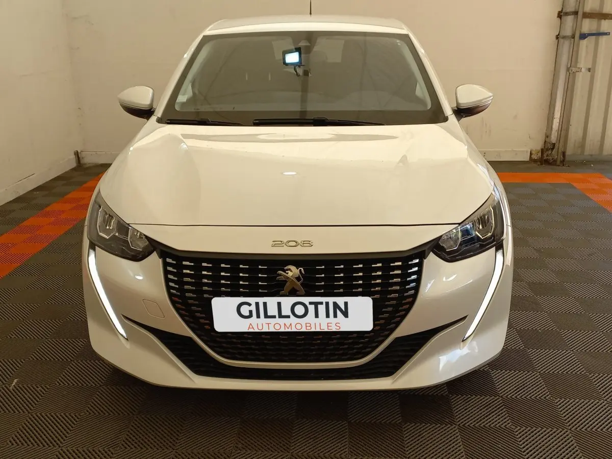 Vue frontale d'une Peugeot 208 PureTech 100 S&S Allure blanche avec calandre noire et feux LED en forme de griffes.