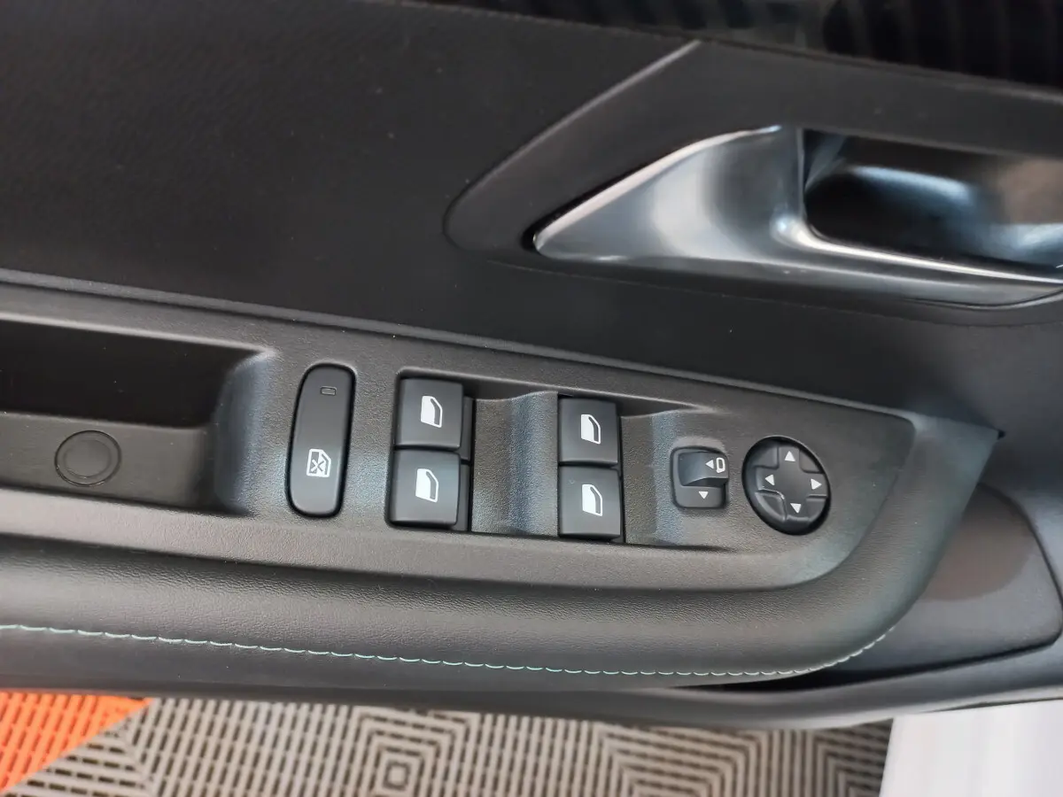 Gros plan sur la commande des vitres et rétroviseurs côté conducteur de la Peugeot 208 blanche, intérieur noir.