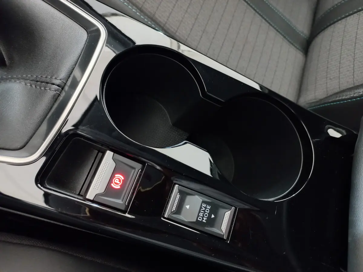 Gros plan sur la console centrale noire brillante de la Peugeot 208 blanche, avec frein à main électrique et bouton Drive Mode.