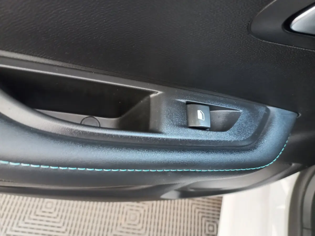 Détail de la commande de lève-vitre sur la porte côté conducteur d'une Peugeot 208 blanche avec surpiqûres bleues.