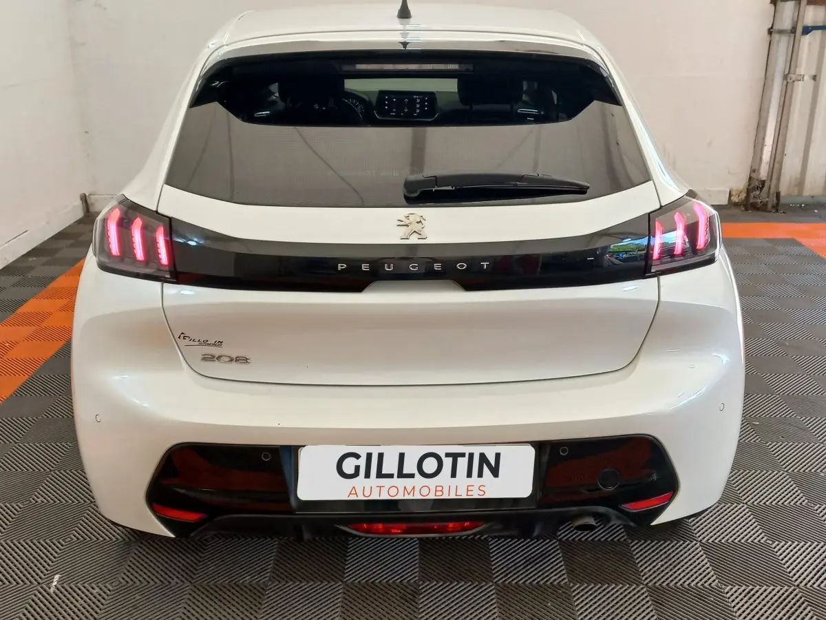 Vue arrière d'une Peugeot 208 blanche avec feux LED allumés et logo Peugeot visible sur le hayon.