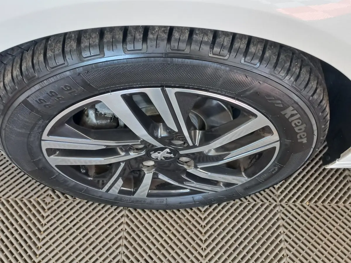 Gros plan sur la jante alliage noire et argentée d'une Peugeot 208 blanche, vue côté gauche arrière.