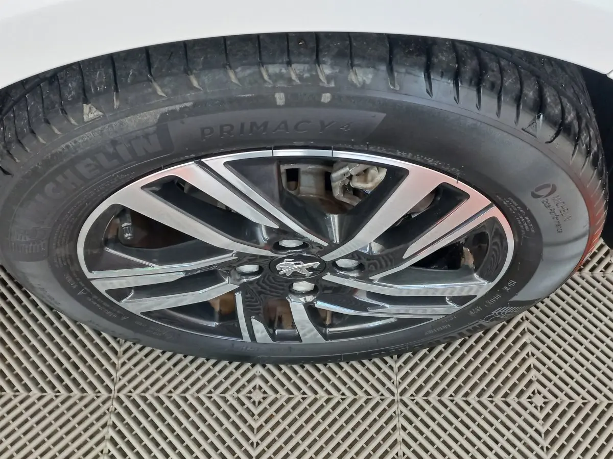 Gros plan sur la jante alliage noire et argentée avec logo Peugeot, pneu Michelin Primacy 4 sur Peugeot 208 blanc.
