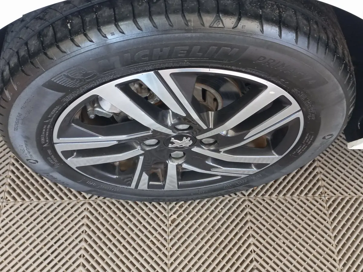 Gros plan sur la roue avant gauche blanche d'une Peugeot 208 PureTech 100 S&S Allure avec jante alliage noire et argentée.