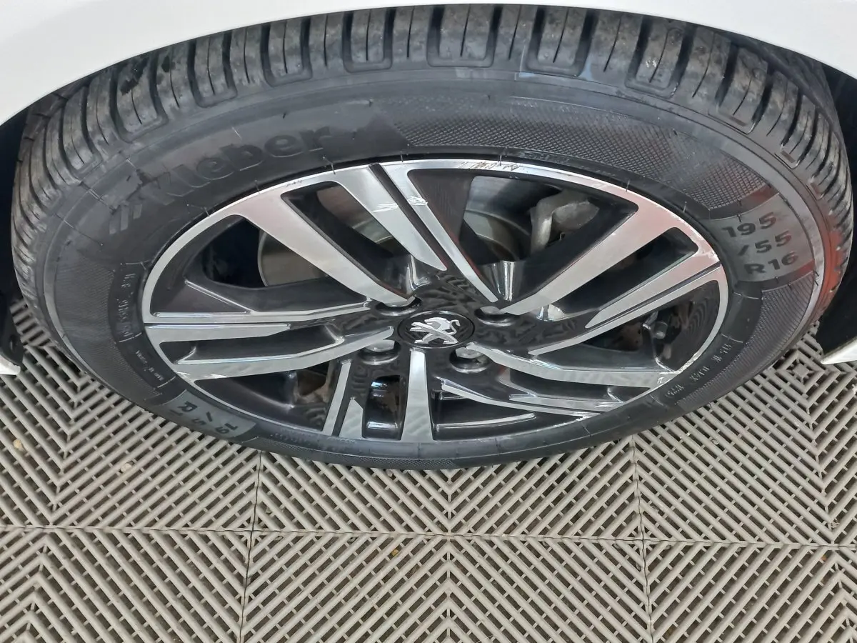 Gros plan sur la jante alliage noire et argentée avec logo Peugeot d'une roue arrière d'une 208 blanche