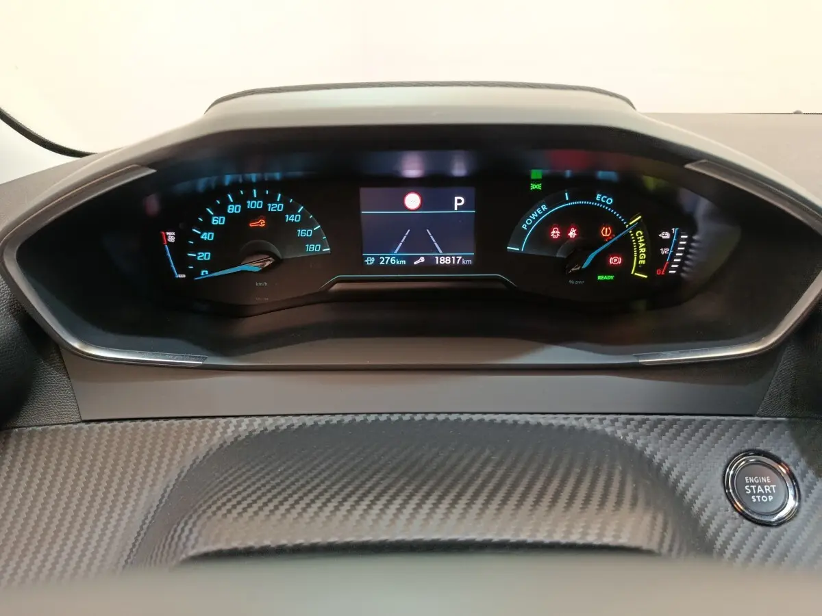 Tableau de bord de Peugeot 208 électrique blanc, vue frontale centrée sur l'affichage numérique et le bouton start/stop.