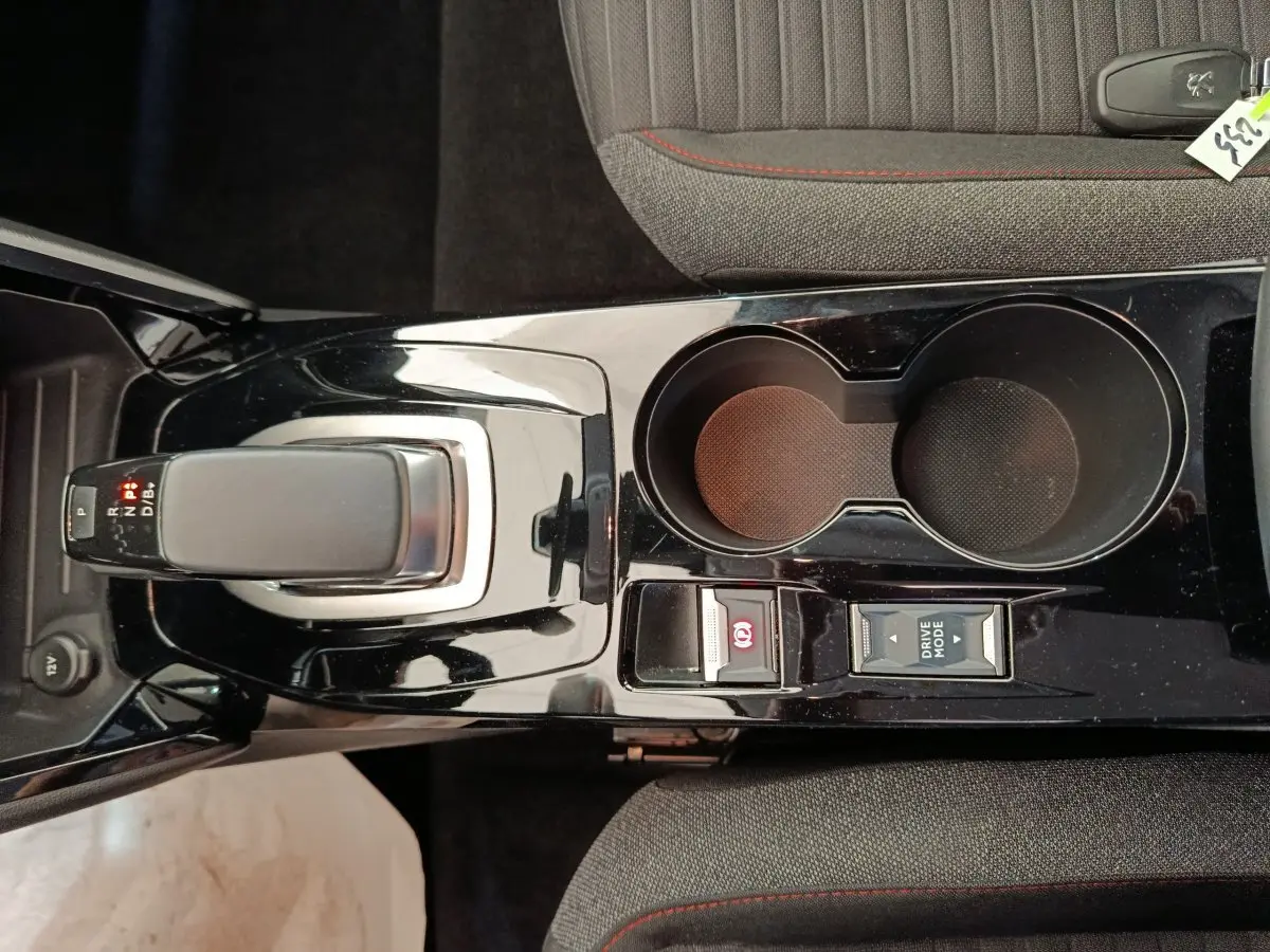 Vue plongeante sur la console centrale noire brillante de la Peugeot 208 électrique avec levier de vitesses et porte-gobelets.