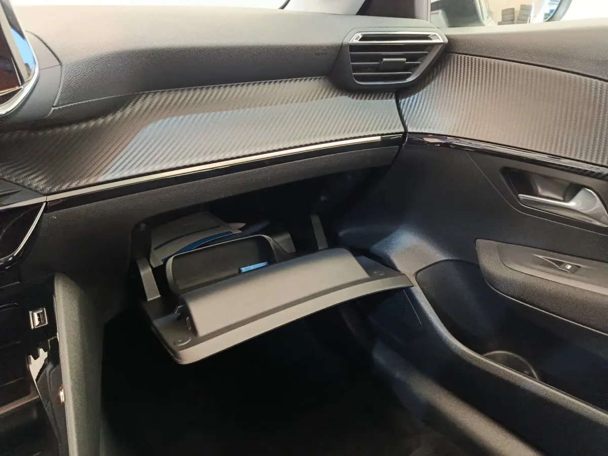 Vue intérieure côté passager du tableau de bord noir avec boîte à gants ouverte du Peugeot 208 électrique blanc 2021.