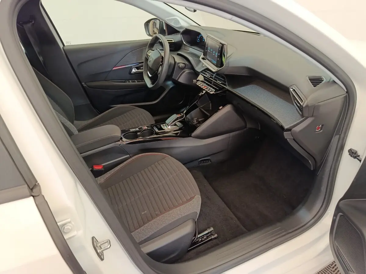 Intérieur côté conducteur de la Peugeot 208 électrique blanche, avec tableau de bord moderne et écran tactile central.