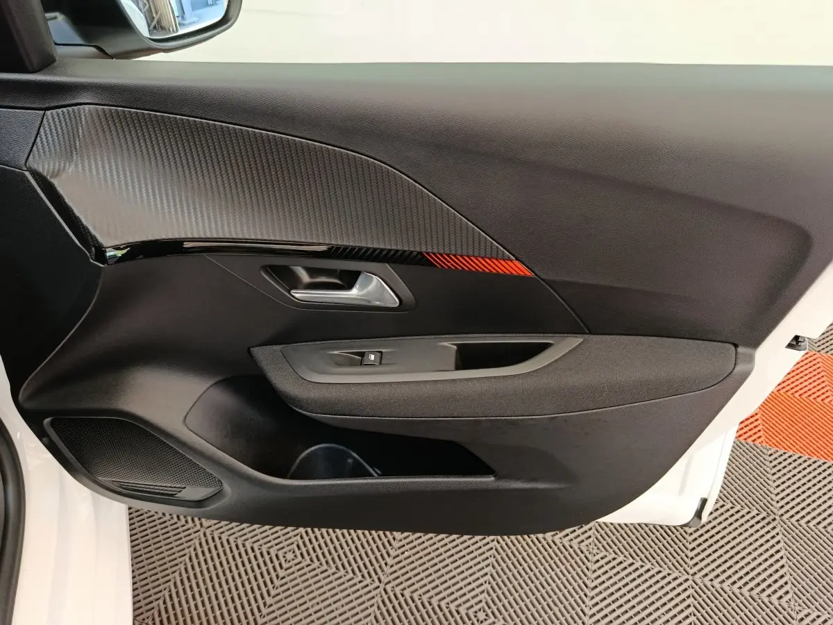 Gros plan sur la porte intérieure côté conducteur de la Peugeot 208 électrique blanche, avec insert noir et détail rouge.