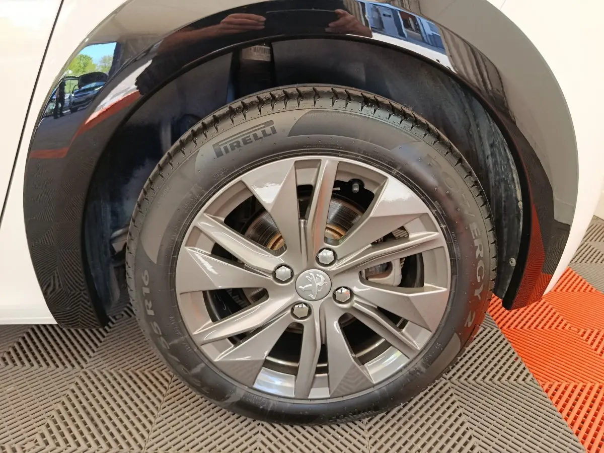 Gros plan sur la roue avant droite de la Peugeot 208 électrique blanche, avec jante alliage et pneu Pirelli.