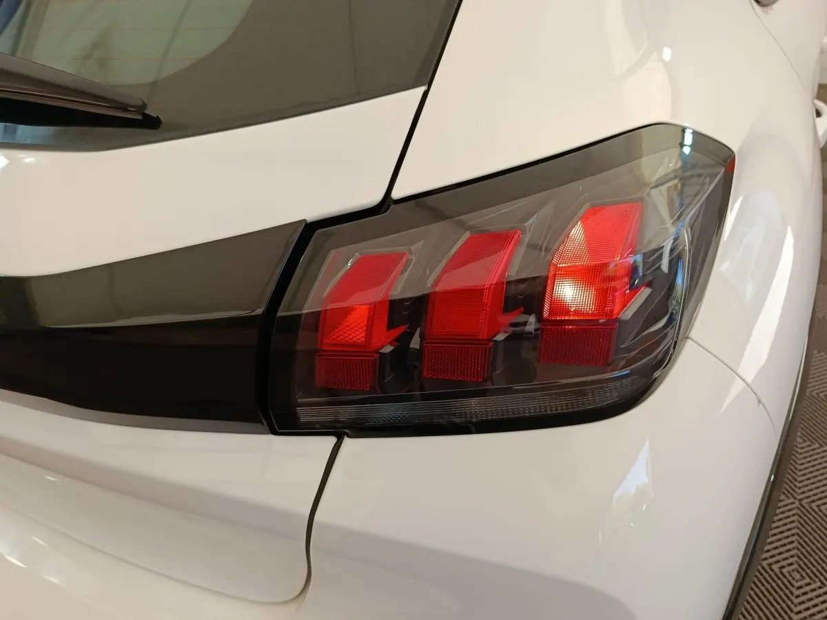 Gros plan sur le feu arrière droit rouge d'une Peugeot 208 électrique blanche, soulignant le design moderne.