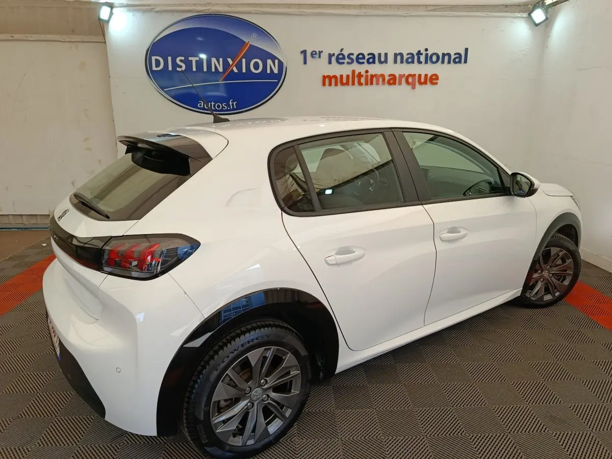 Peugeot 208 électrique blanc vue 3/4 arrière droit en intérieur avec jantes foncées et feux arrière LED distinctifs.