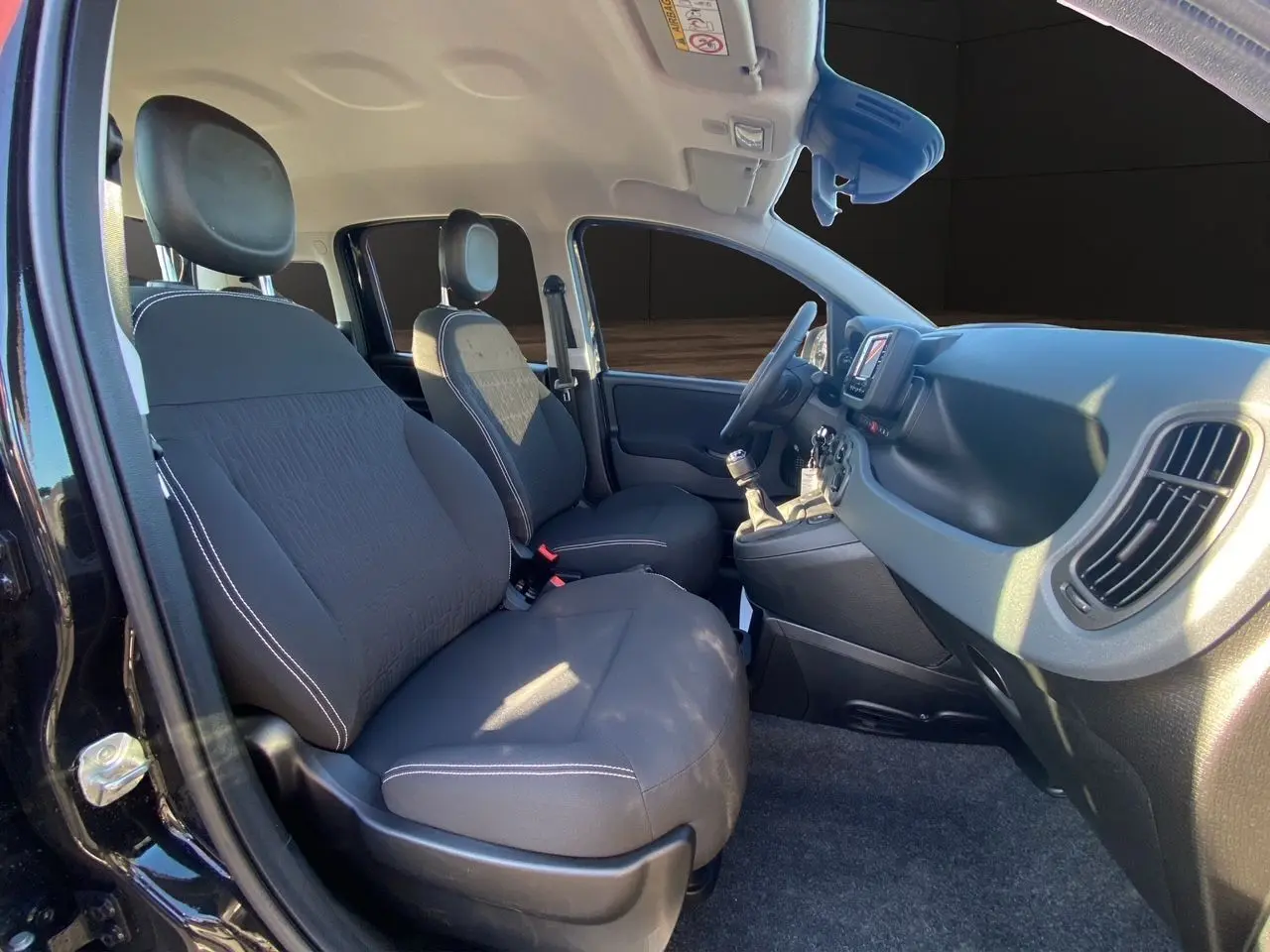 Intérieur avant noir de la Fiat Panda 2025, vue côté gauche montrant sièges, volant et tableau de bord avec écran tactile.