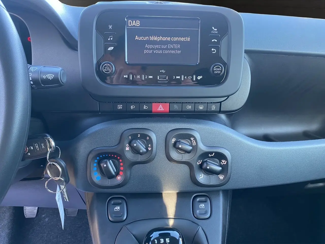 Tableau de bord et console centrale du Fiat Panda noir 2025, avec écran multimédia et commandes de climatisation visibles.