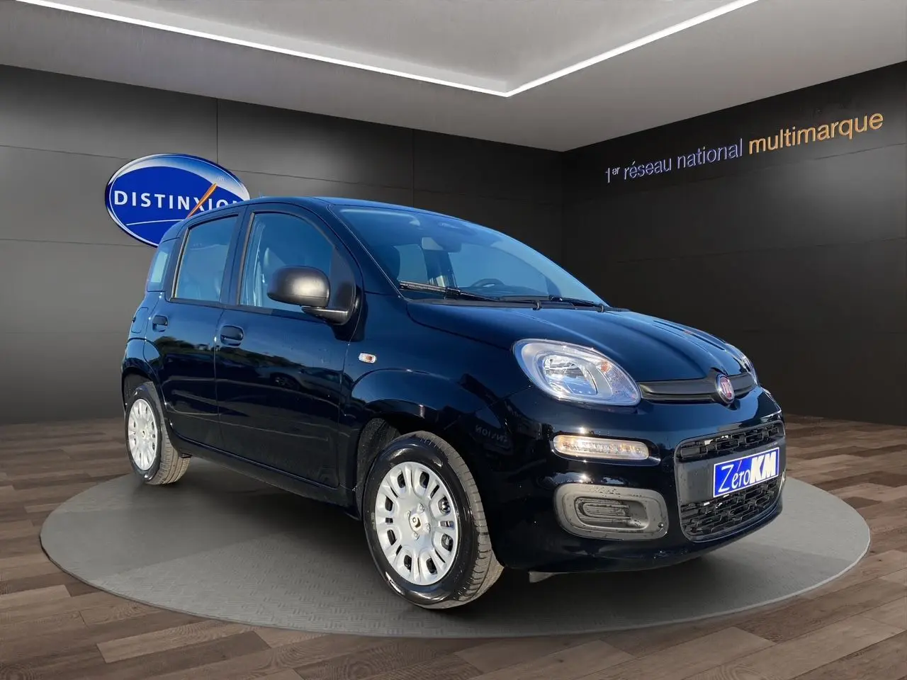 Fiat Panda noire vue en 3/4 avant droit, avec phares allumés et jantes argentées, en showroom.