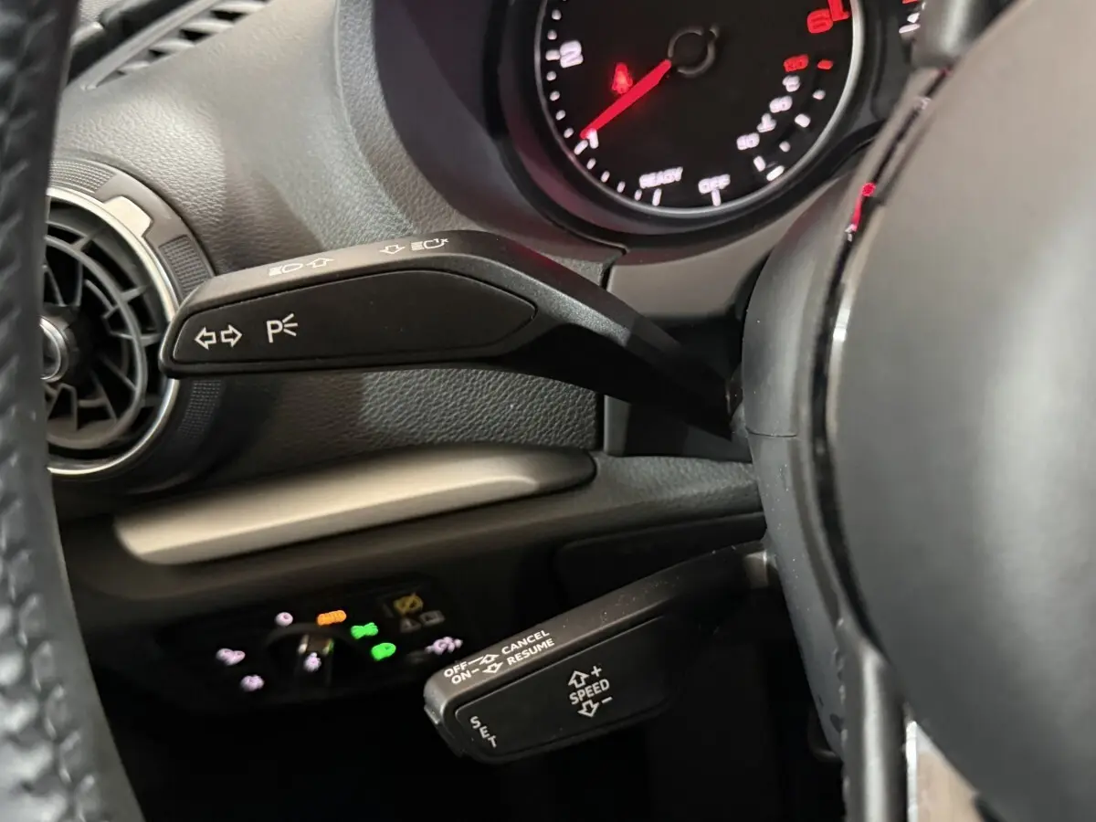 Gros plan sur les commandes au volant d'une Audi A3 bleu 2018, mettant en valeur les leviers de clignotants et régulateur de vitesse.