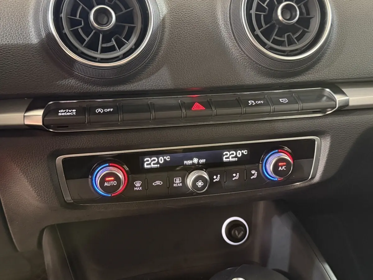 Détail de la console centrale de l'Audi A3 bleu, avec climatisation bi-zone réglée à 22°C et aérateurs ronds noirs.
