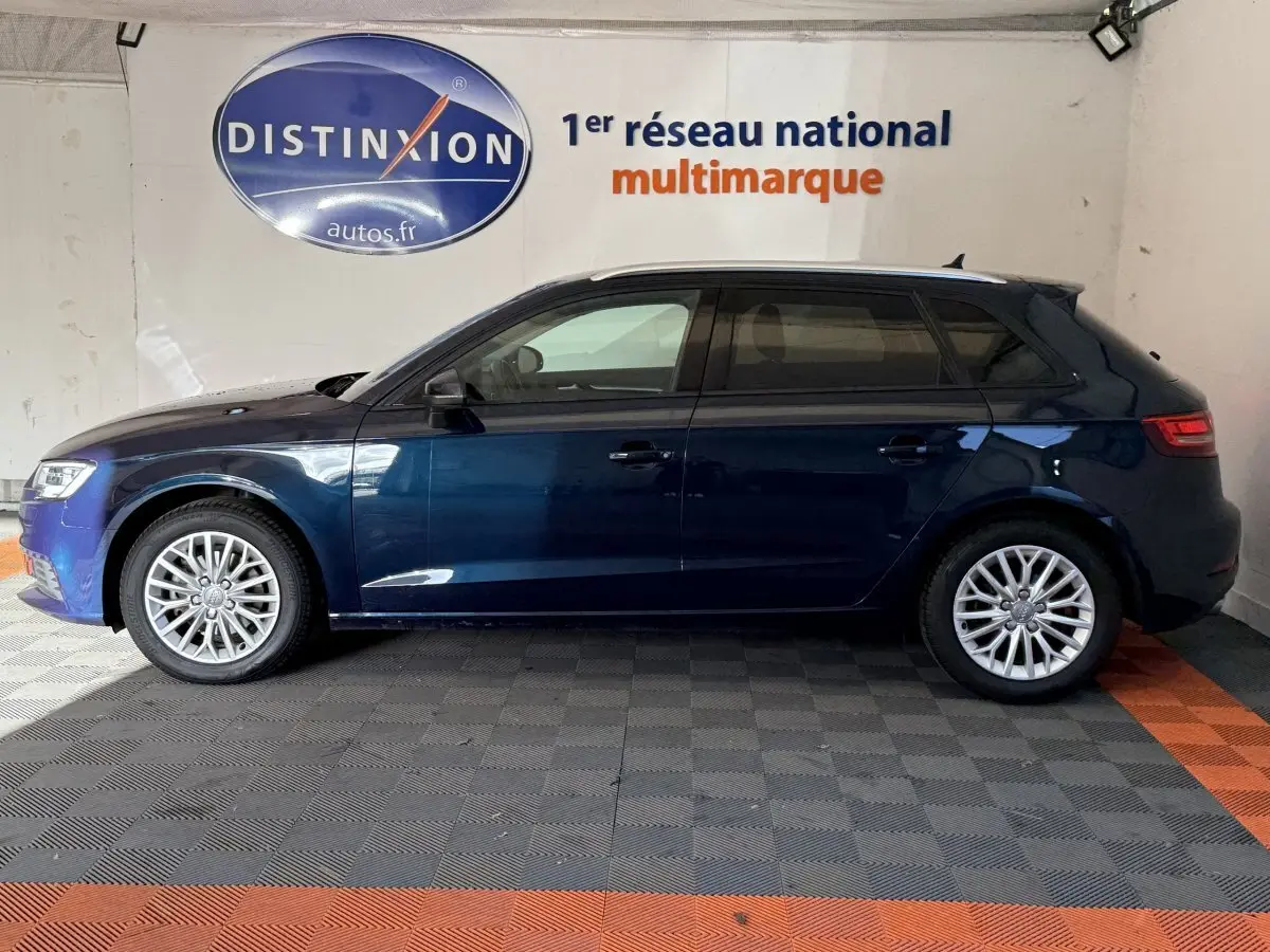 Profil côté gauche d'une Audi A3 bleu foncé 2018 garée en intérieur sur sol à damiers gris et orange.