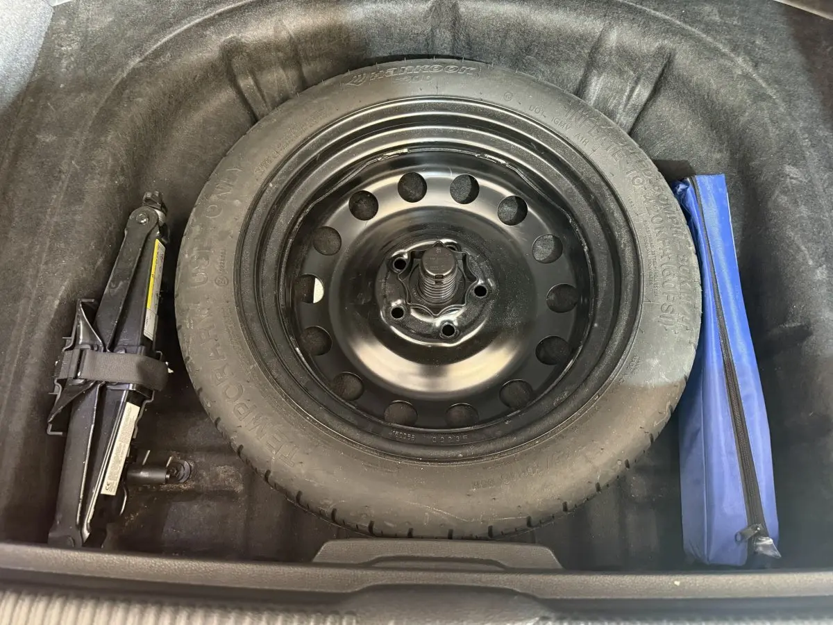 Vue rapprochée de la roue de secours galette noire et du cric dans le coffre d'une Audi A3 bleu 2.0 TDI 2018.