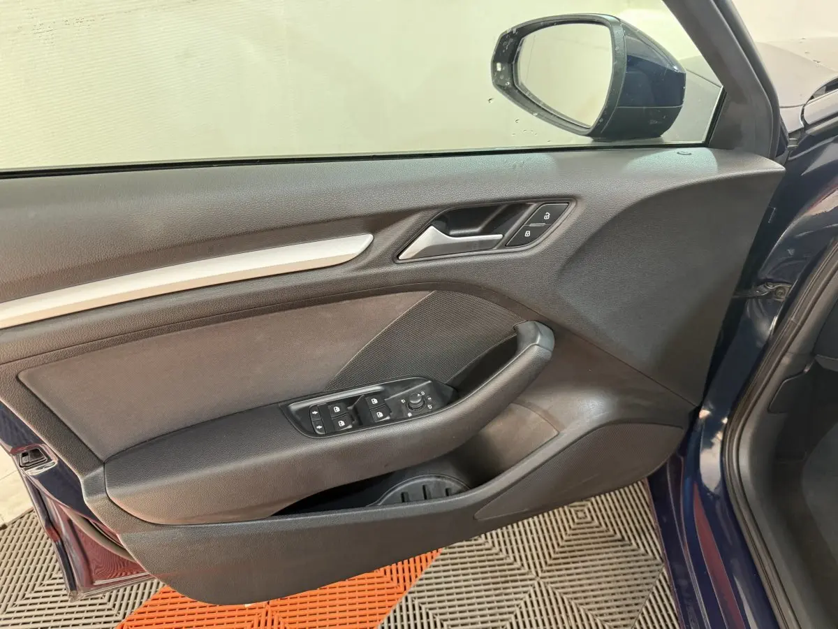 Vue rapprochée de la porte avant gauche d'une Audi A3 bleu 2018, avec commandes électriques et miroir extérieur visible.