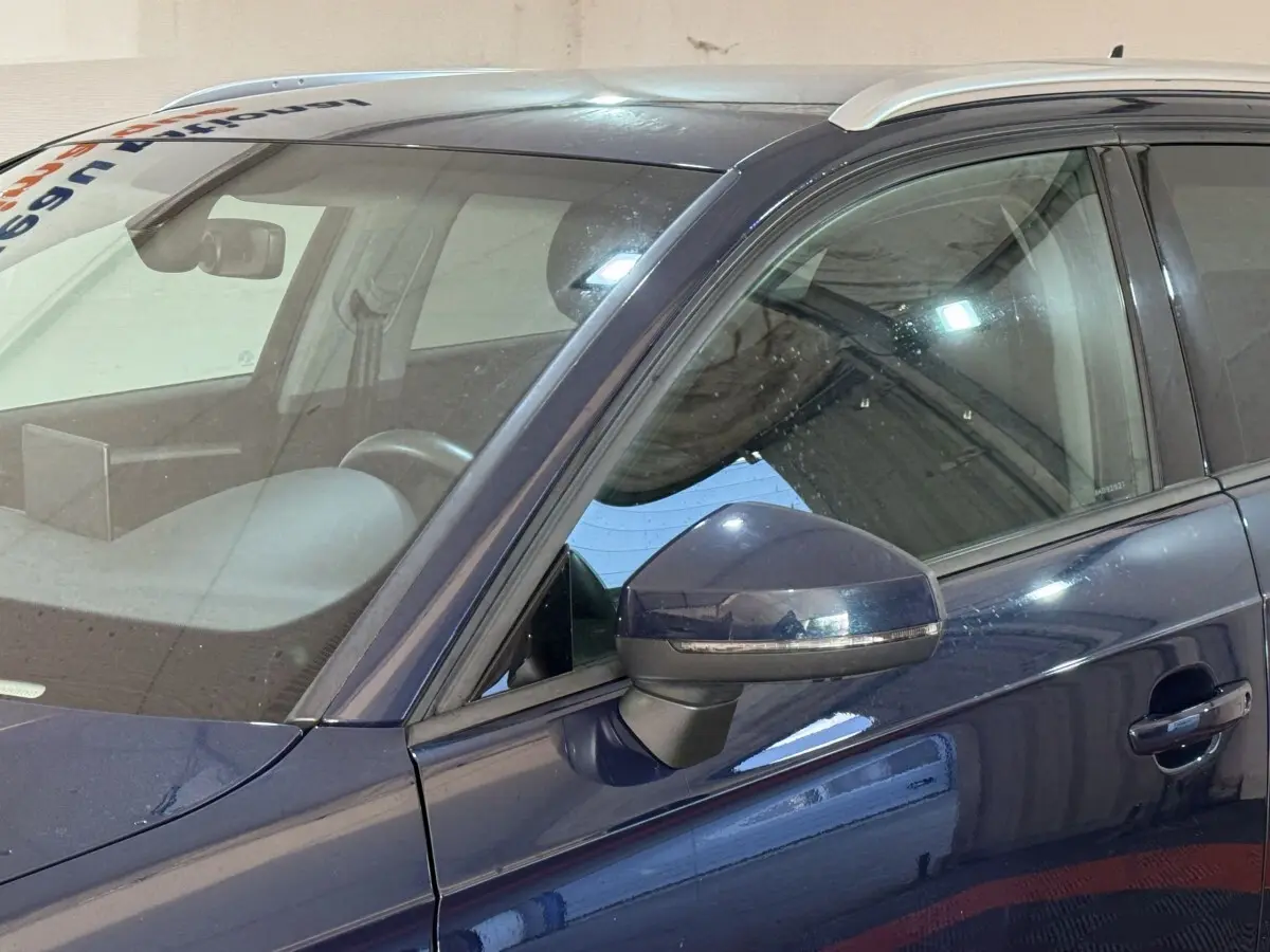 Vue latérale gauche rapprochée d'une Audi A3 bleu foncé avec rétroviseur et poignée de porte visibles.