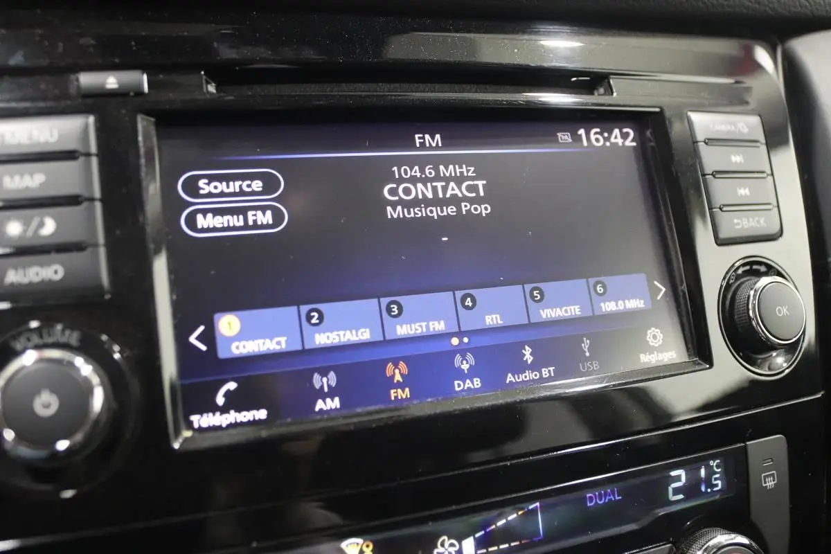 Gros plan sur l'écran multimédia et la console centrale du Nissan X-Trail 1.7 D 150, affichant la radio FM et la climatisation digitale.