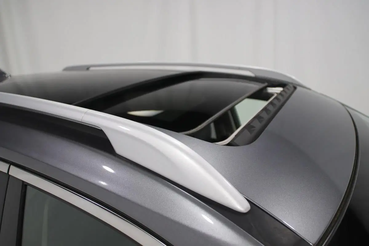 Détail du toit ouvrant ouvert et des barres de toit sur un Nissan X-TRAIL gris métallisé.