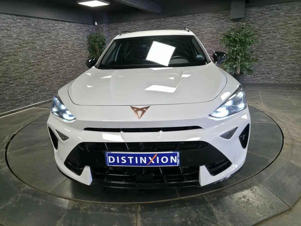 Vue avant d'une CUPRA Formentor blanche avec phares allumés et calandre noire dans un showroom intérieur.