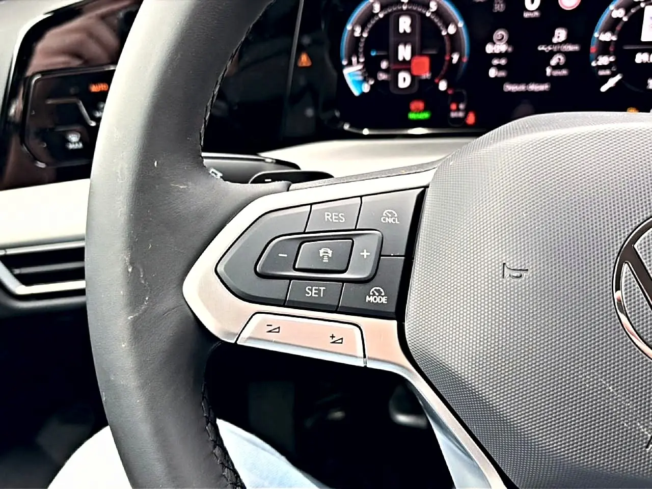 Gros plan sur le volant noir de la Volkswagen Golf 2026, avec commandes de régulateur de vitesse et tableau de bord numérique en arrière-plan.