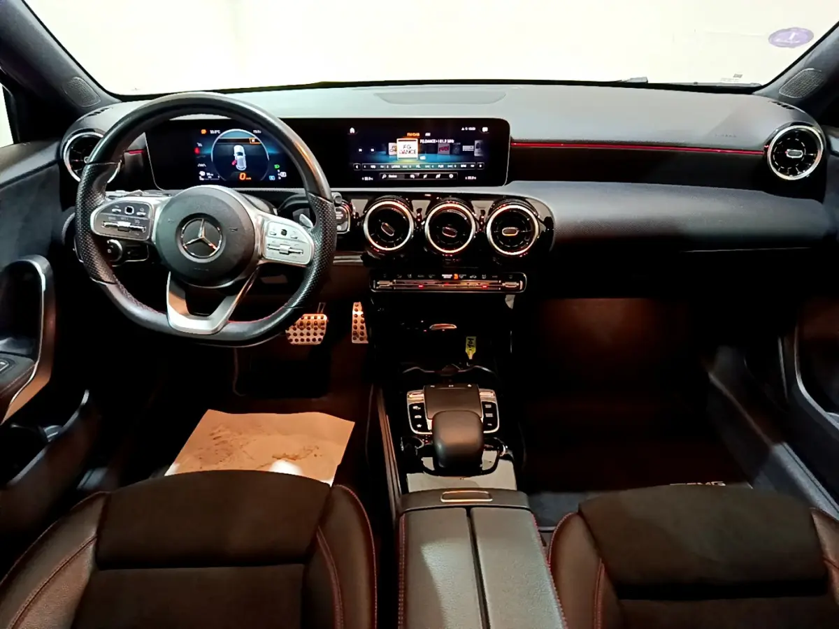 Vue intérieure avant de la Mercedes Classe A 180 AMG Line 2019, tableau de bord noir avec éclairage rouge et volant cuir multifonction.