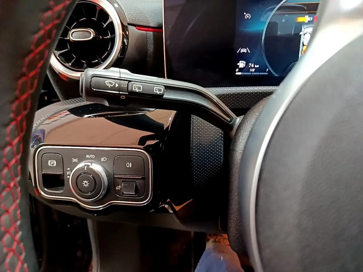 Gros plan sur la commande d’éclairage et le volant cuir noir avec surpiqûres rouges côté gauche d’une Mercedes Classe A A 180 AMG Line 2019.