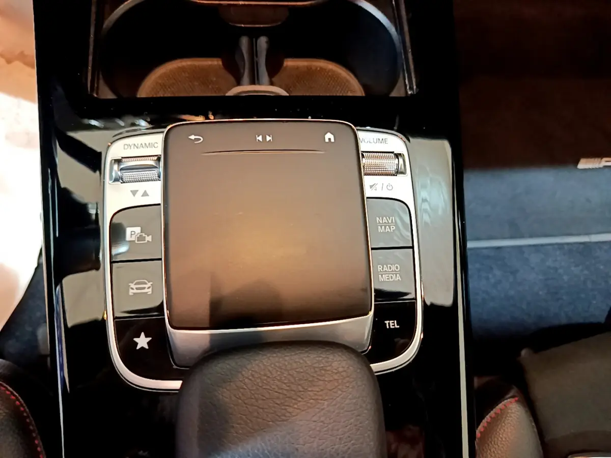 Gros plan sur la console centrale noire brillante de la Mercedes Classe A 180 AMG Line avec pavé tactile et commandes multimédia.